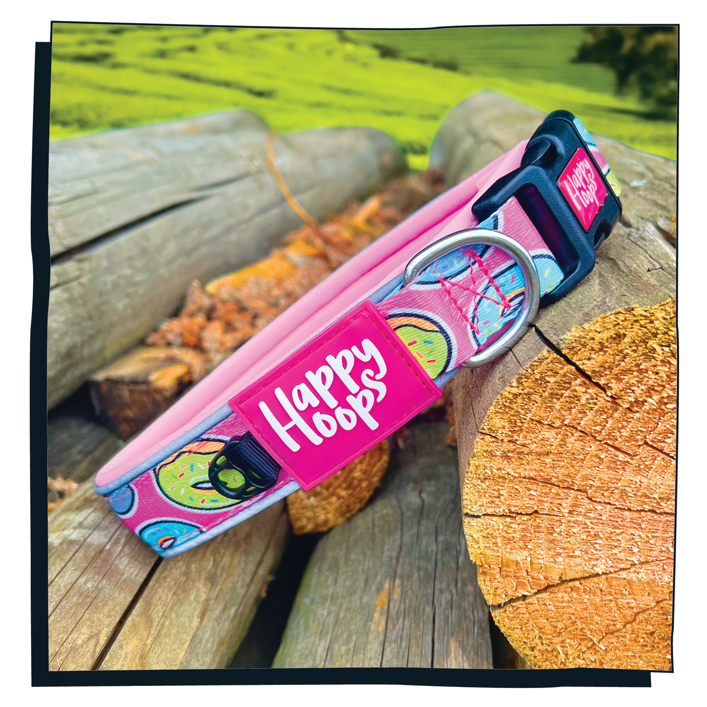 Pink dog collar with 'Happy Hoops' label on wooden logs